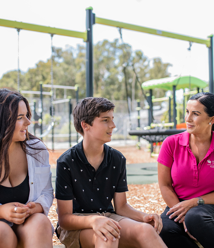 A Challenge community Services team member sits with a boy and a woman at a park