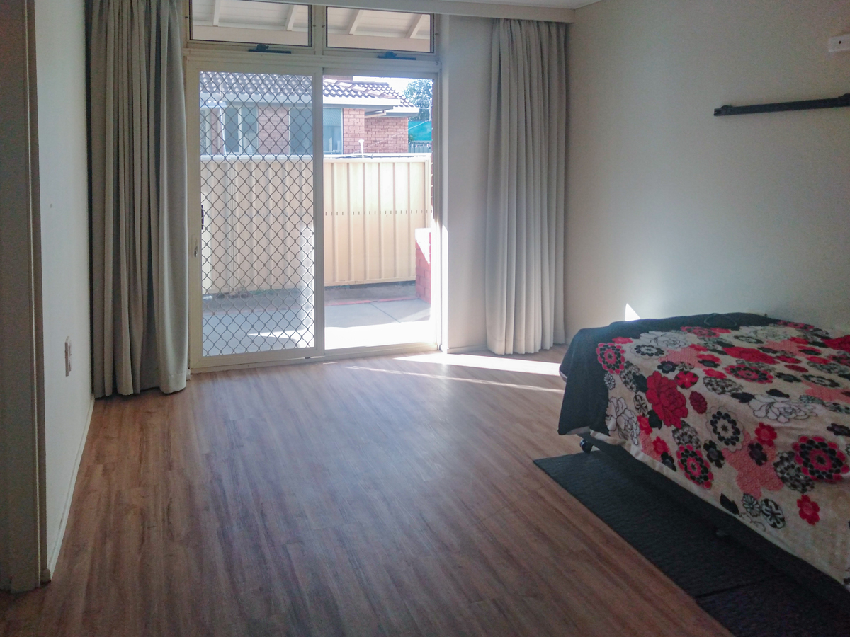Bedroom - Timber look flooring, off-white walls and a large glass sliding door with security screen and blackout curtains, A single bed with a colurful beadspread can be seen in the right hand corner