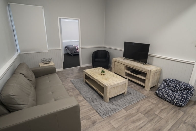 Loungeroom of the Challenge Community Services Respite Care accomodation featuring timber look flooring, stylish timber furniture, a leather lounge and a TV