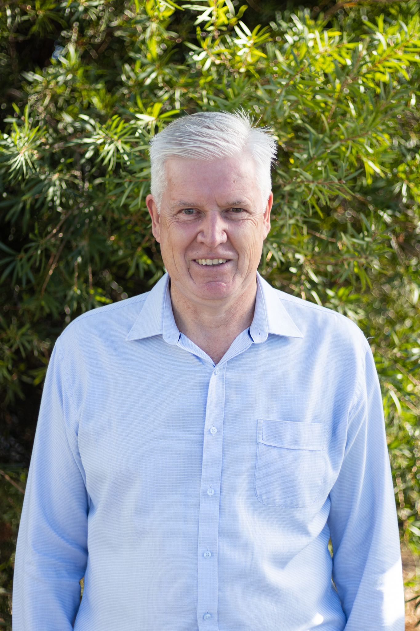 Andrew Corbett - Executive team member and General Manager People, Culture and Safety for Challenge Community Services. Andrew is standing in front of some greenery wearing a light blue business shirt.