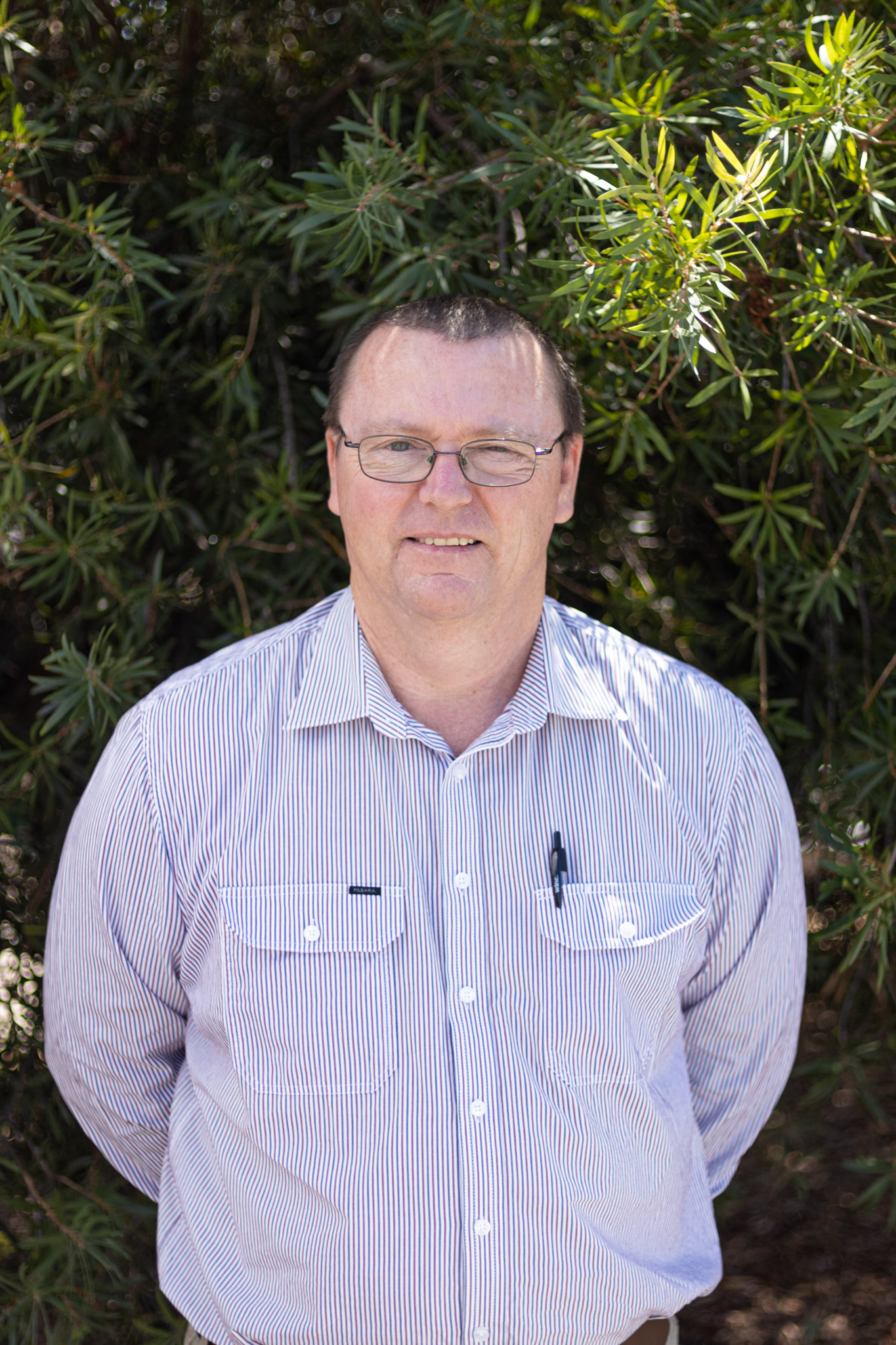 Richard Hardwick - General Manager of Business Services at Challenge Community Services. Richard wears a blue business shirt and stands in front of some greenery.