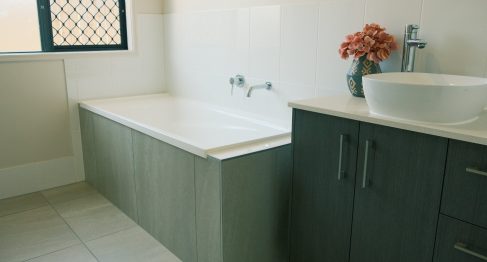 Bright modern bathroom with a single bath and vanity. There are flowers in a vase on the counter top.